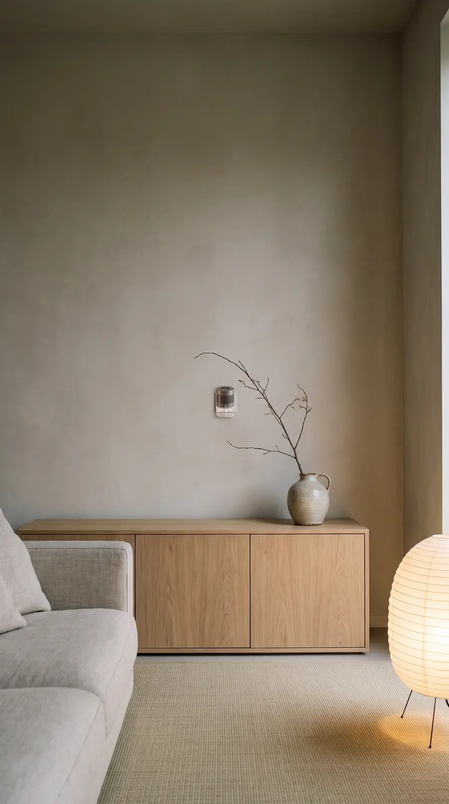 Salon japandi : buffet en chêne clair, vase en céramique, canapé en lin et lampe en papier. Un diffuseur MOSK anthracite est fixé au mur au-dessus du buffet.